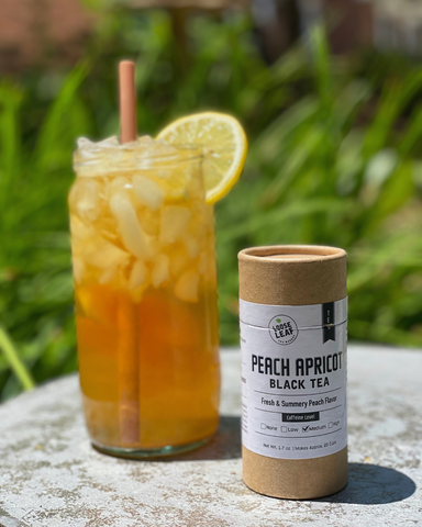 peach apricot black tea canister next to brewed peach arnold palmer iced tea with fresh lemon and straw in natural setting