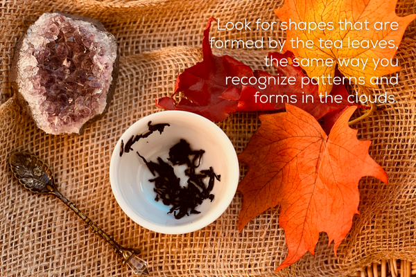 Tea leaves in a white cup, with a crystal, spoon, and autumn leaves.