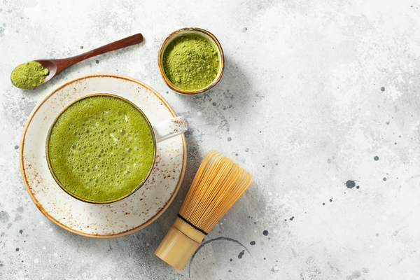 matcha latte with whisk, powder and spoon in a kitchen setting