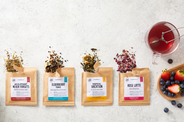 Four tea pouches with a cup of tea and fresh berries.