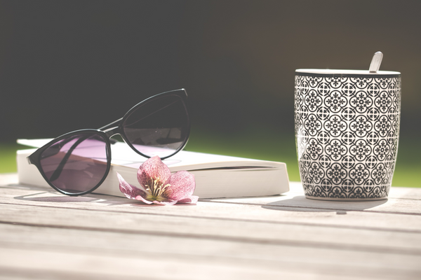 Cup of tea with book, sunglasses, and fresh flower.