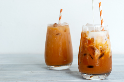 brewed iced black tea with milk and striped paper straw and white background