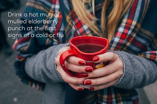 Woman wearing shawl holding a mug of mulled elderberry punch.