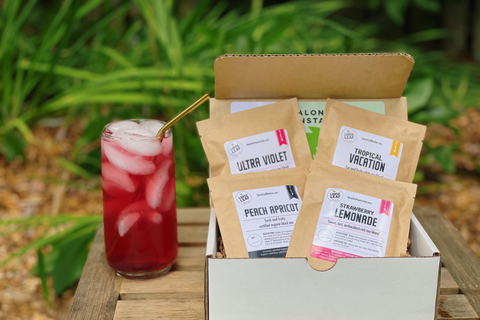 box with four summer loose leaf teas in an outdoor setting next to a bright red, brewed iced tea