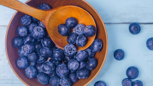 wood bowl with fresh blueberries and wooden spoon