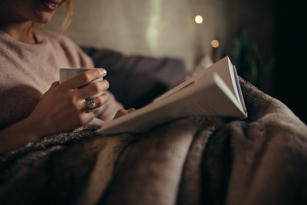 woman drinking herbal tea for sleep and reading to promote better sleep