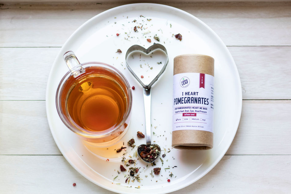 A cup of tea and a canister of I Heart Pomegranates tea on a plate.