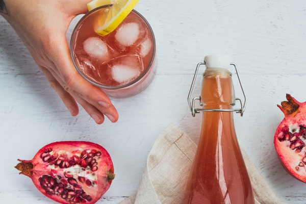 Kombucha in a bottle and over ice, with fresh pomegranates.