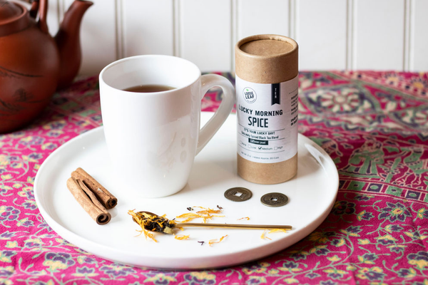 Lucky Morning Spice tea with white cup and saucer, with spoon, and assorted items.