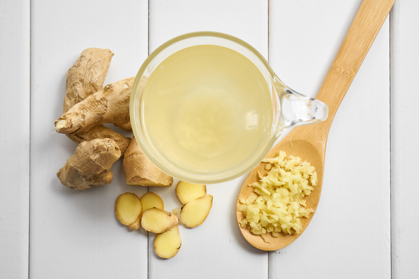 ginger tea with fresh grated ginger on a wooden spoon and whole large piece of ginger