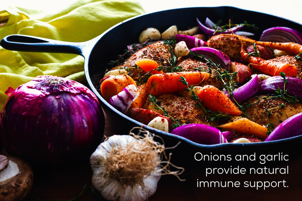 Onion and garlic next to a skillet of autumn veggies.