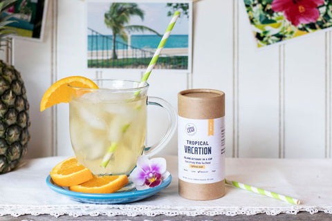 tropical vacation tea blend freshly brewed next to canister at a beach house, with freshly sliced oranges