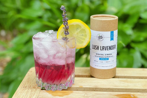 lavender layered mocktail topped with sparkling water with Lush Lavender blend on the side in a natural setting