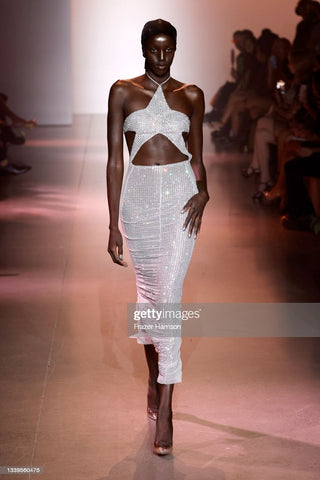 Woman walking on  a runway with a silver mermaid dress that has cut outs around the neckline that make the shape of a star