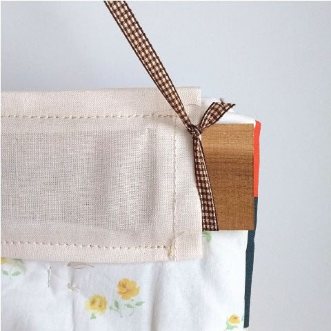 Insert a dowel or wooden rod in the hanging sleeve and attach a ribbon to each end