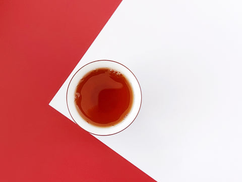 A close-up photo of BESTLEAFTEA's Jinjunmei black tea, with dark, twisted leaves and a deep amber brew in a white ceramic cup