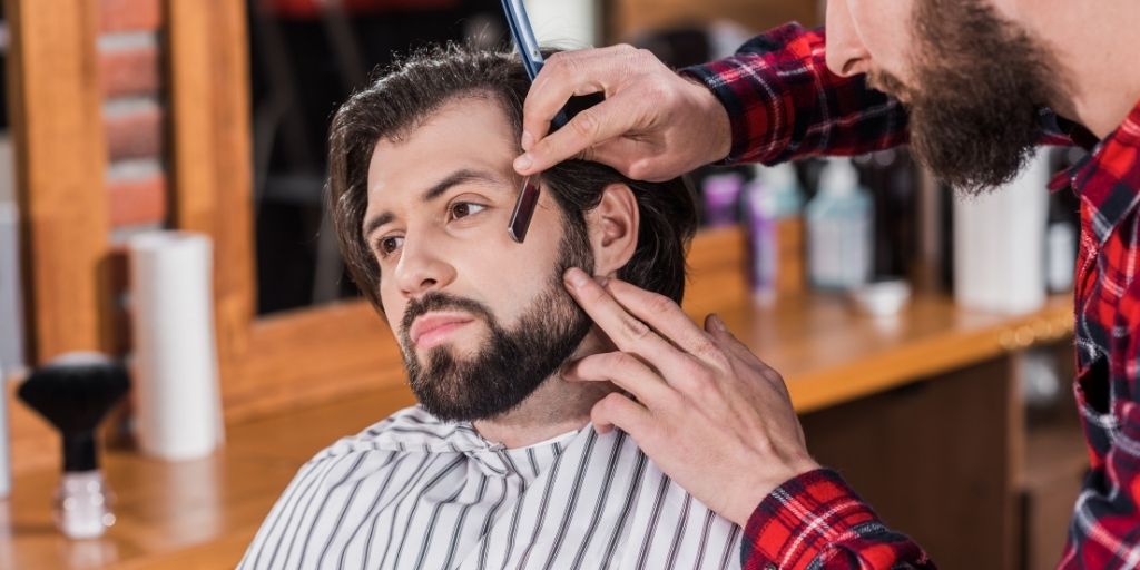 Barber shaving a man's sideburn