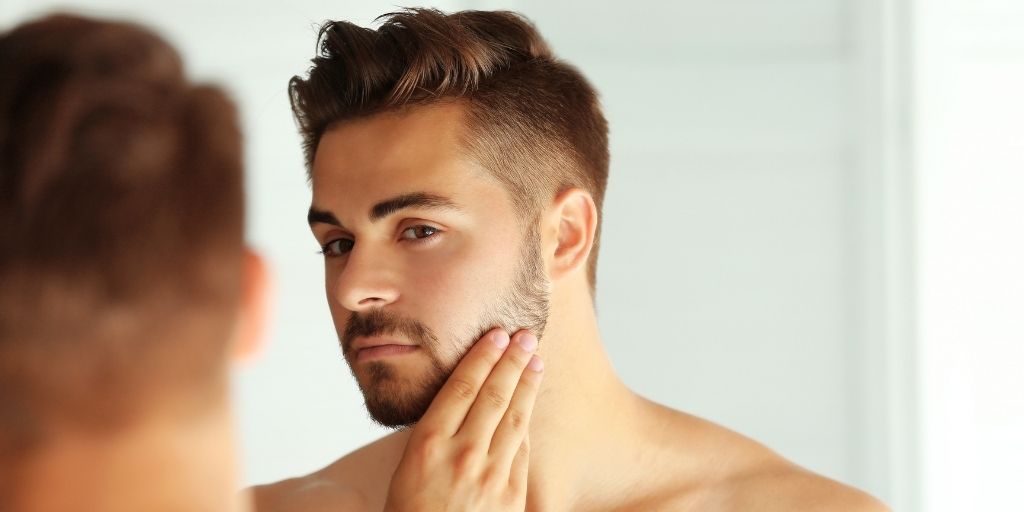 Man Assessing His Face and Beard in the Mirror