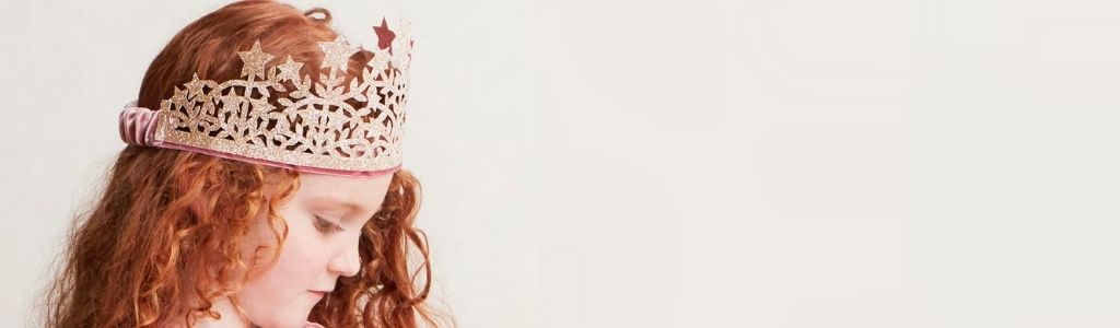 An image of a young girl with red curly hair, wearing a pink glitter princess tiara