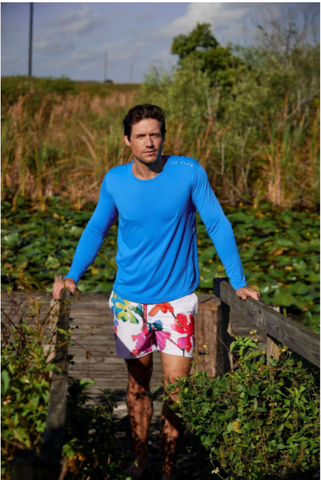 man in blue shirt standing in field in le club swim trunks