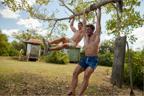 two men swinging from tree in le club original swim trunks