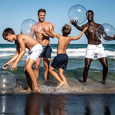 group friends in trunks play on beach