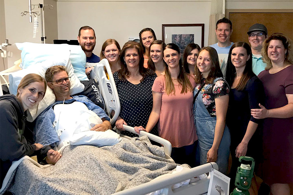 Austin Patten in hospoital bed surrounded by wife Jill and large group of friends.