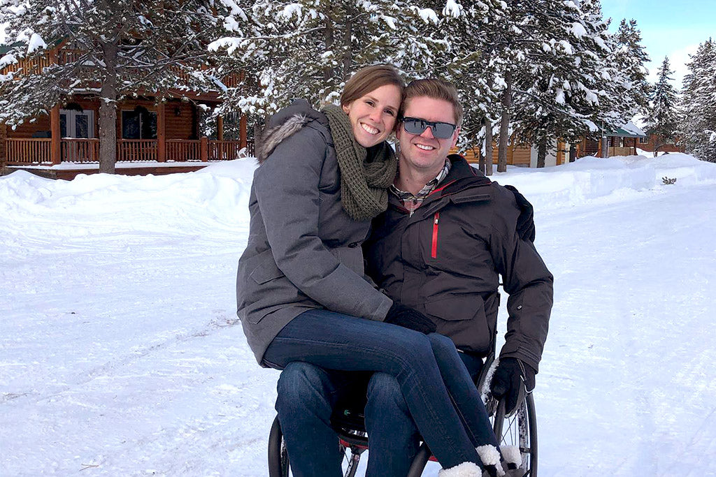 Jill Patten sitting in Austins lap as he sits in a wheelchair in a winter snowy setting.