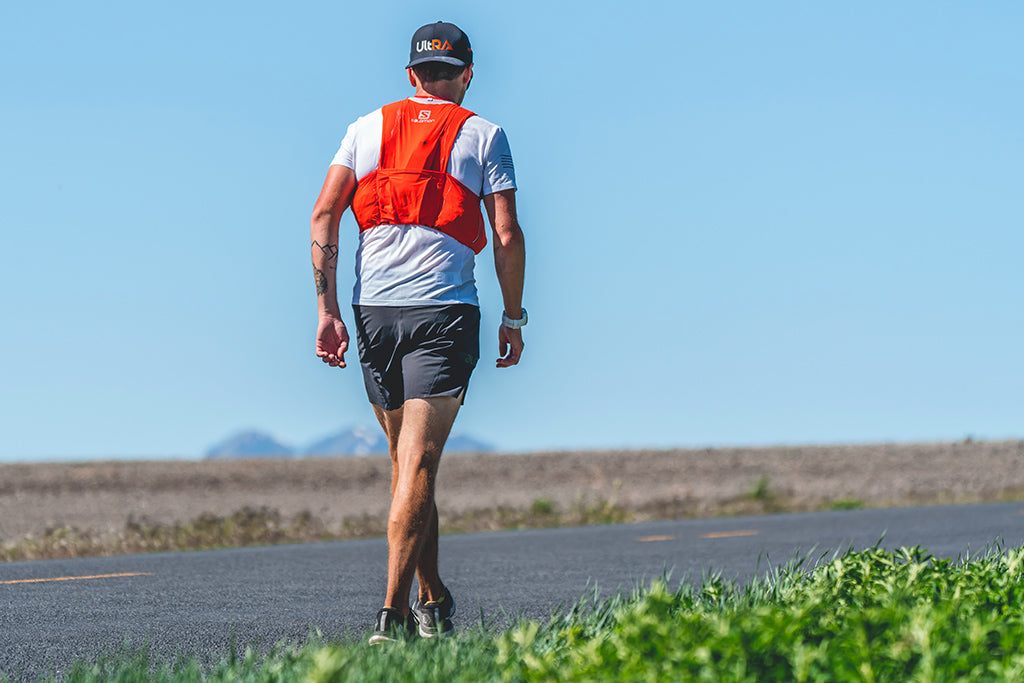Endurance athlete Michael Mcknight wearing solomon vest and Kogalla Ultra hat running on long Cache Valley incline road.