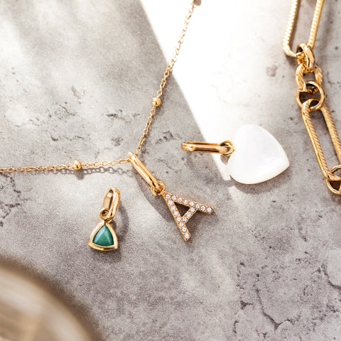 How to clean gold jewellery at home: A picture containing ‘A’ initial pendant, emerald gemstone and moonstone birthstone pendant
