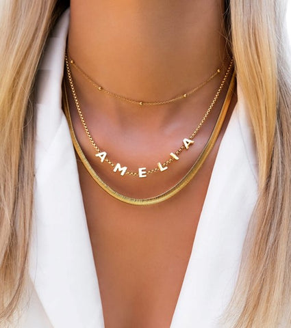 how to get custom jewellery made; a woman wearing a gold custom name necklace layered with other gold necklaces