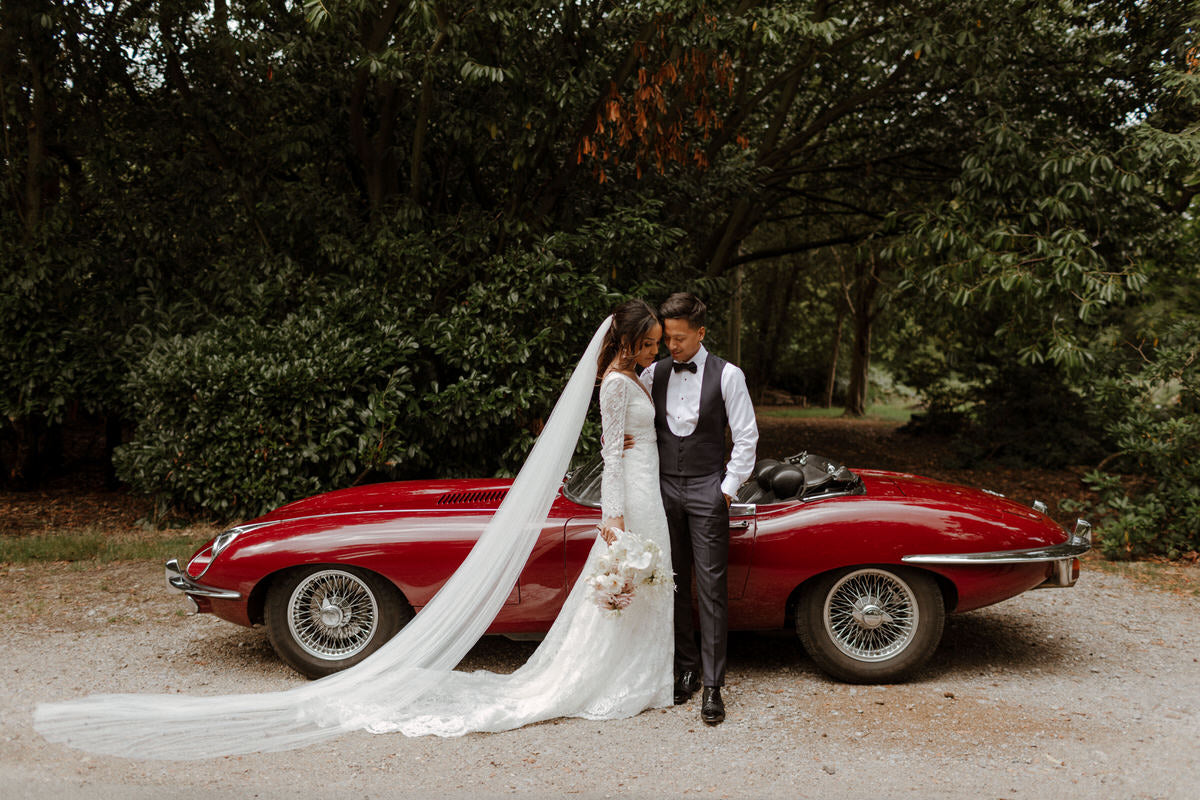 Bride and groom stand in front of their wedding car, a Jaguar E-type.