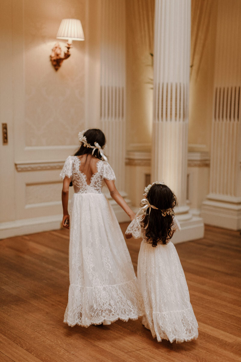 Flower girls wearing our Violette full length lace flower girl dress and flower crowns of fresh roses. Shown from the back showing the feature eyelash lace back.