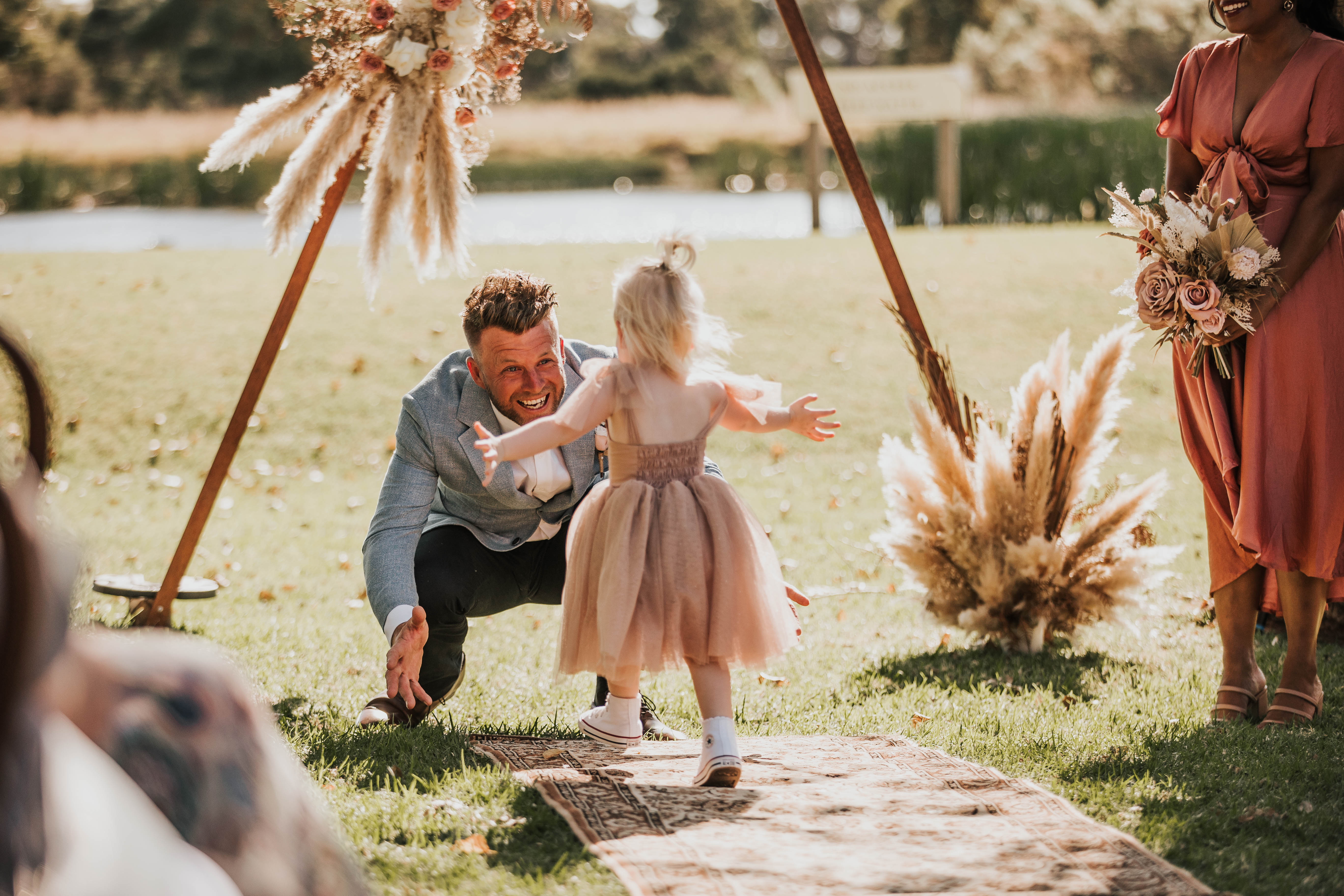A flower girl runs up the aisle into the arms of Groom Andrew. She wears our Rosie flower girl dress in Champagne.