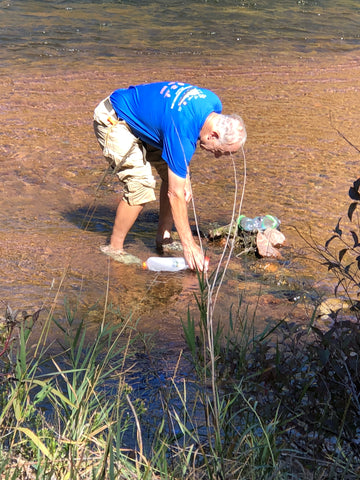 older man standing in river filling up a 2L Vecto