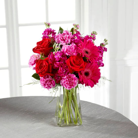 hot pink carnations, red roses, hot pink gerbera daisies in a clear glass vase