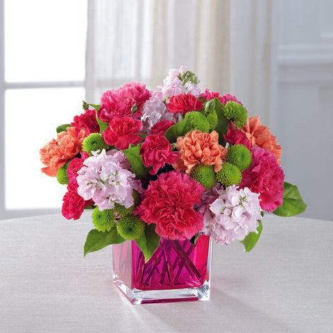 hot pink carnations, orange carnations, light lavender stock, green pompons, in a clear, pink, glass cube