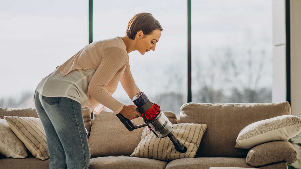 Using a small hand-held vacuum cleaner with brush attachment to clean the blades of the ceiling fan with ease.