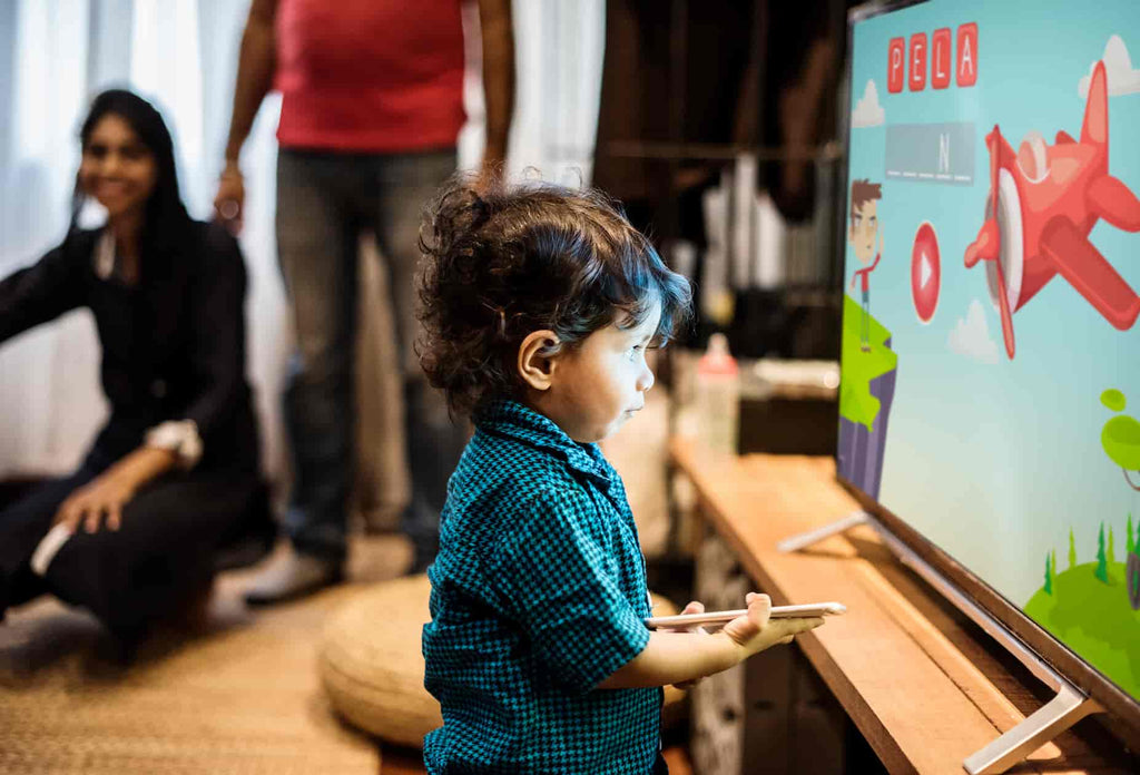 A child playing with the TV remote and TV screen in a curious manner