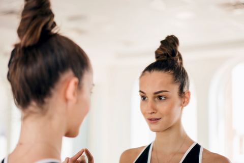 woman looking at mirror with hair in a topknot bun