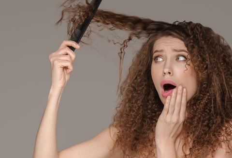 woman combing curly hair and looking surprised