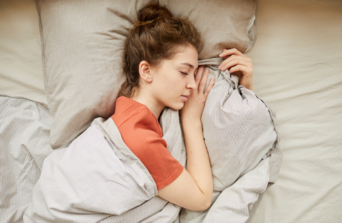 woman with a bun sleeping in bed holding a blanket