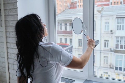 woman looking at hand mirror by the window