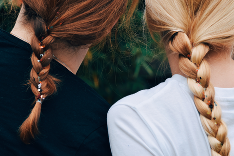 backview of red headed and blonde headed women in braids
