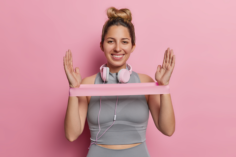 happy woman with headphones stretching a resistance band between arms