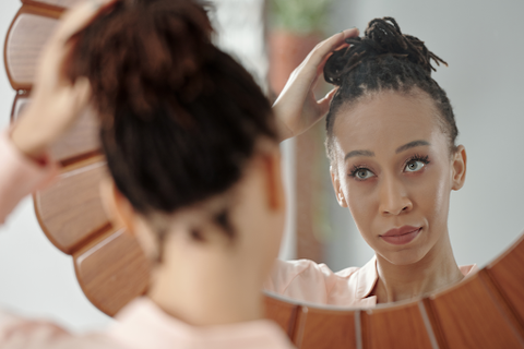 A lady looking in the mirror and putting her hair in a bun on top of her head