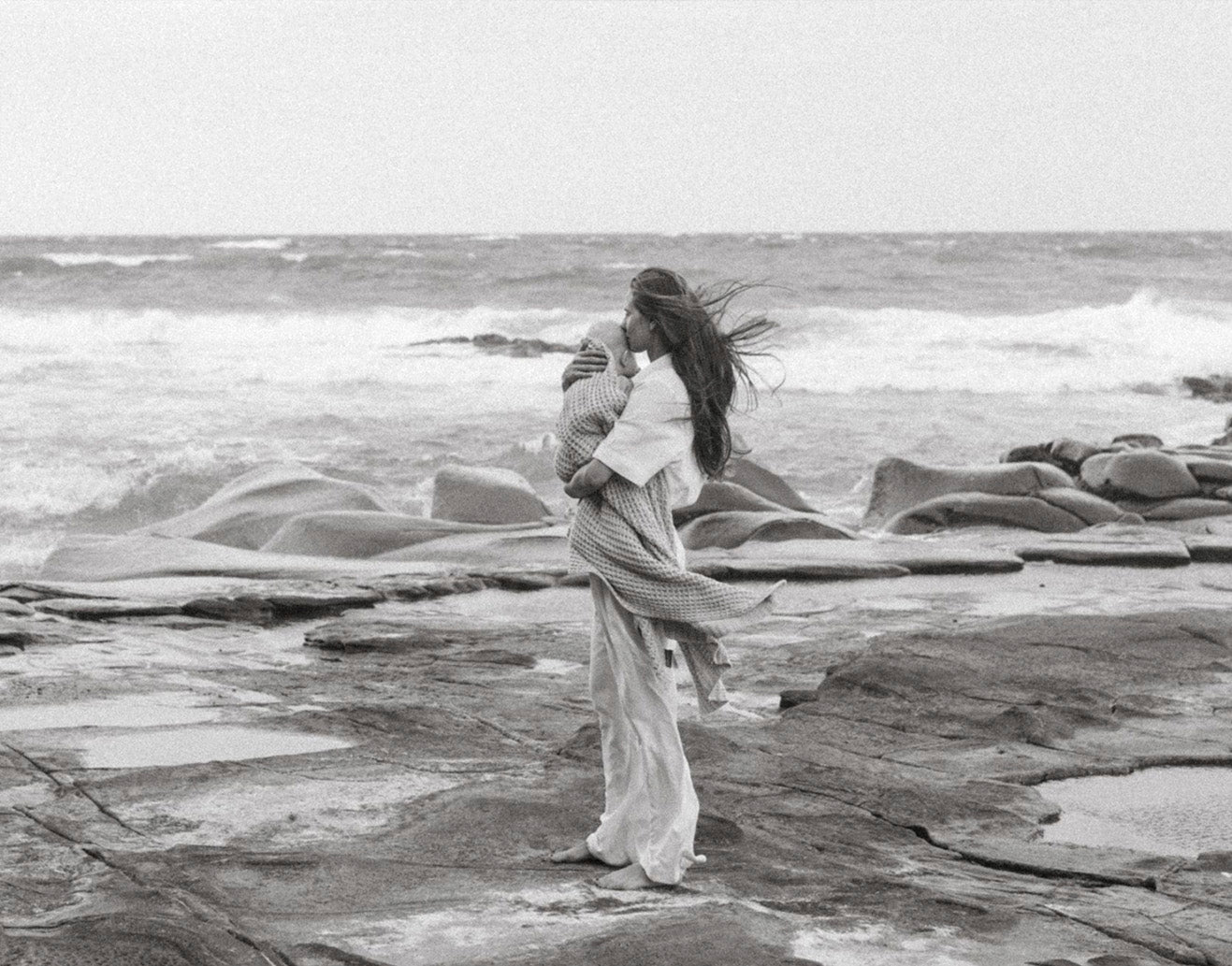 Women kissing her baby on the beach with wind blown hair