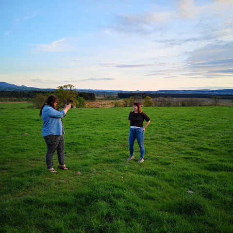 two women stand in a field, one is photographing the other