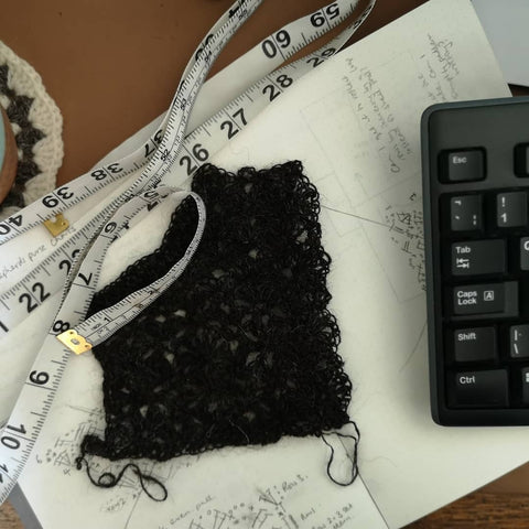 a swatch and tape measure lie next on an open design journal, the edge of a keyboard is in shot