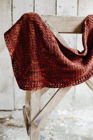 brown thick shawl rests on a carpentry support in a wooden barn